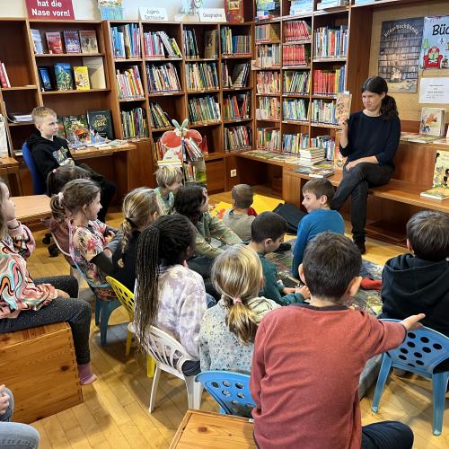 Die Kinder sitzen in der Bücherei vor Katharina, die das Buch "Bitte nicht öffnen - bissig!" vorstellt.