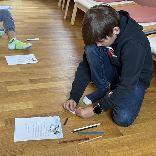 Ein Junge malt nach Vorgabe die Bilder auf einem Blatt an bzw. aus.