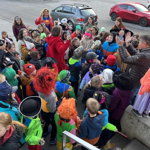 Kinder stehen gesammelt vor dem Gemeindeamt und singen, Bürgermeister macht klatschend mit;