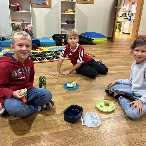 Drei Kinder aus der 2.Klasse sitzen am Boden und jausnen.