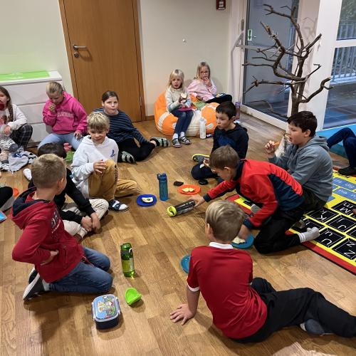 Viele Kinder sitzen am Boden und genießen die gesunde Jause.